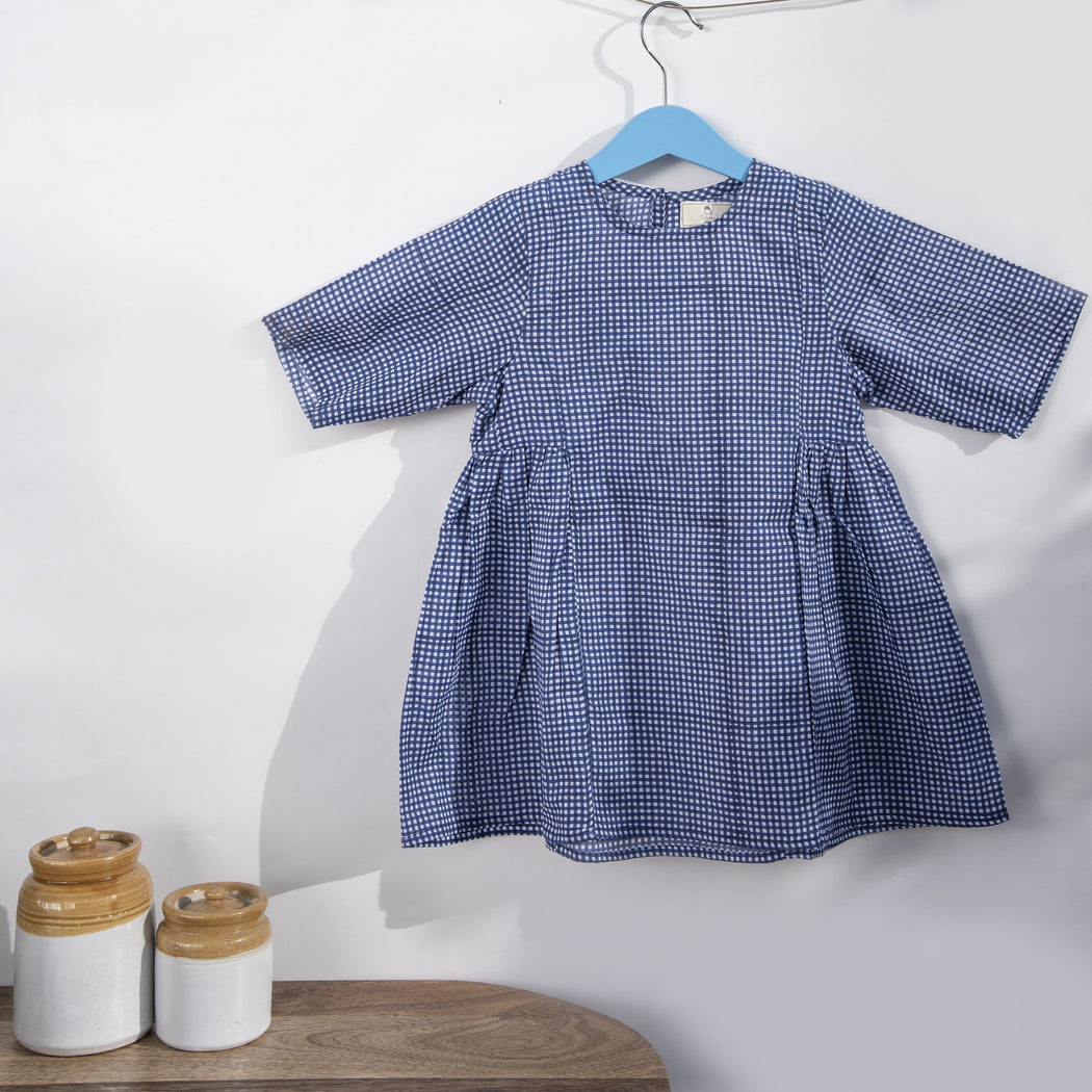 An indigo chequered hand block printed dress in cotton mulmul fabric with a button fastening at the back .This is a slightly loose dress with side gathers.
