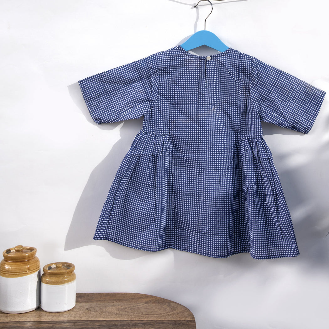 An indigo chequered hand block printed dress in cotton mulmul fabric with a button fastening at the back .This is a slightly loose dress with side gathers.